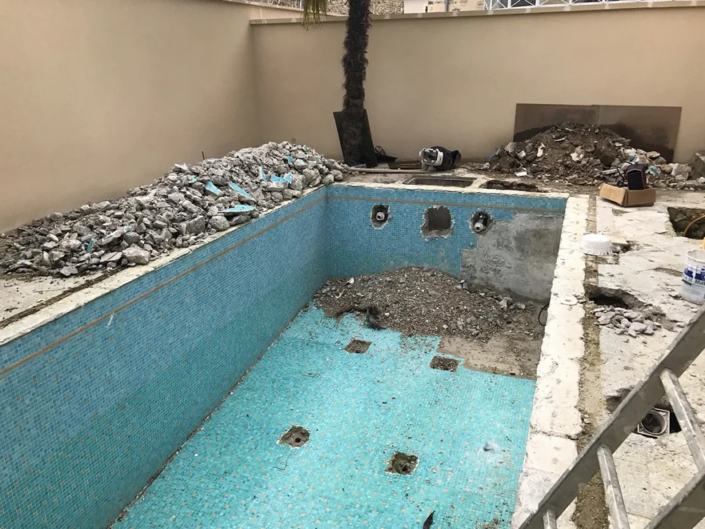 Piscine carrelée en mosaïque turquoise avant rénovation : gravats sur la plage, pièces à sceller déposées