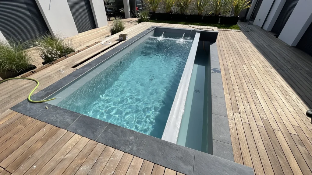 Piscine à revêtement gris clair en cours de remise en eau, lame d'eau, margelles ardoise et terrasse en bois, chantier à Milly-la-Forêt