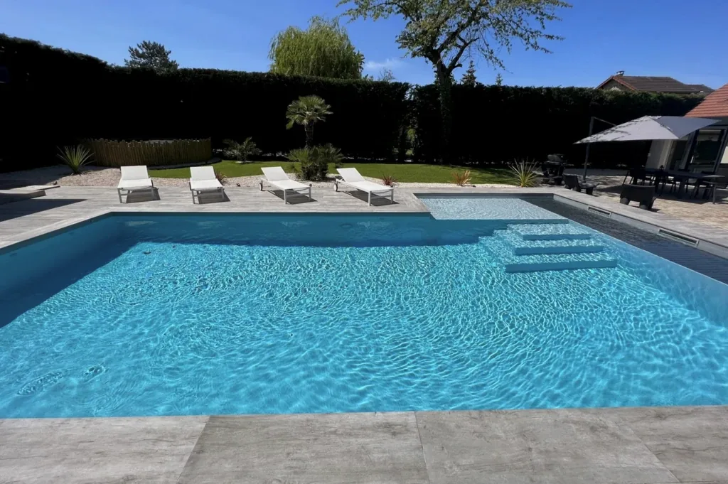 Piscine rectangulaire à l'eau claire avec plage immergée et marches, transats sur un dallage imitation bois